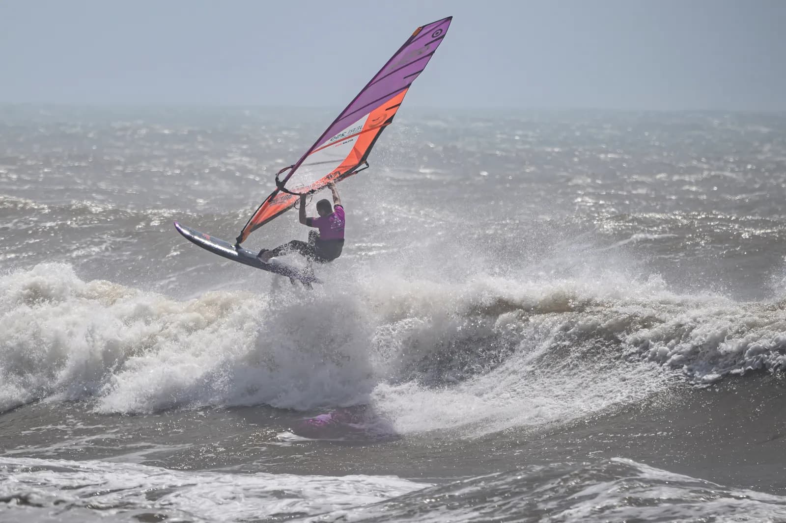 Rider with a purple sail hitting the lip of a wave